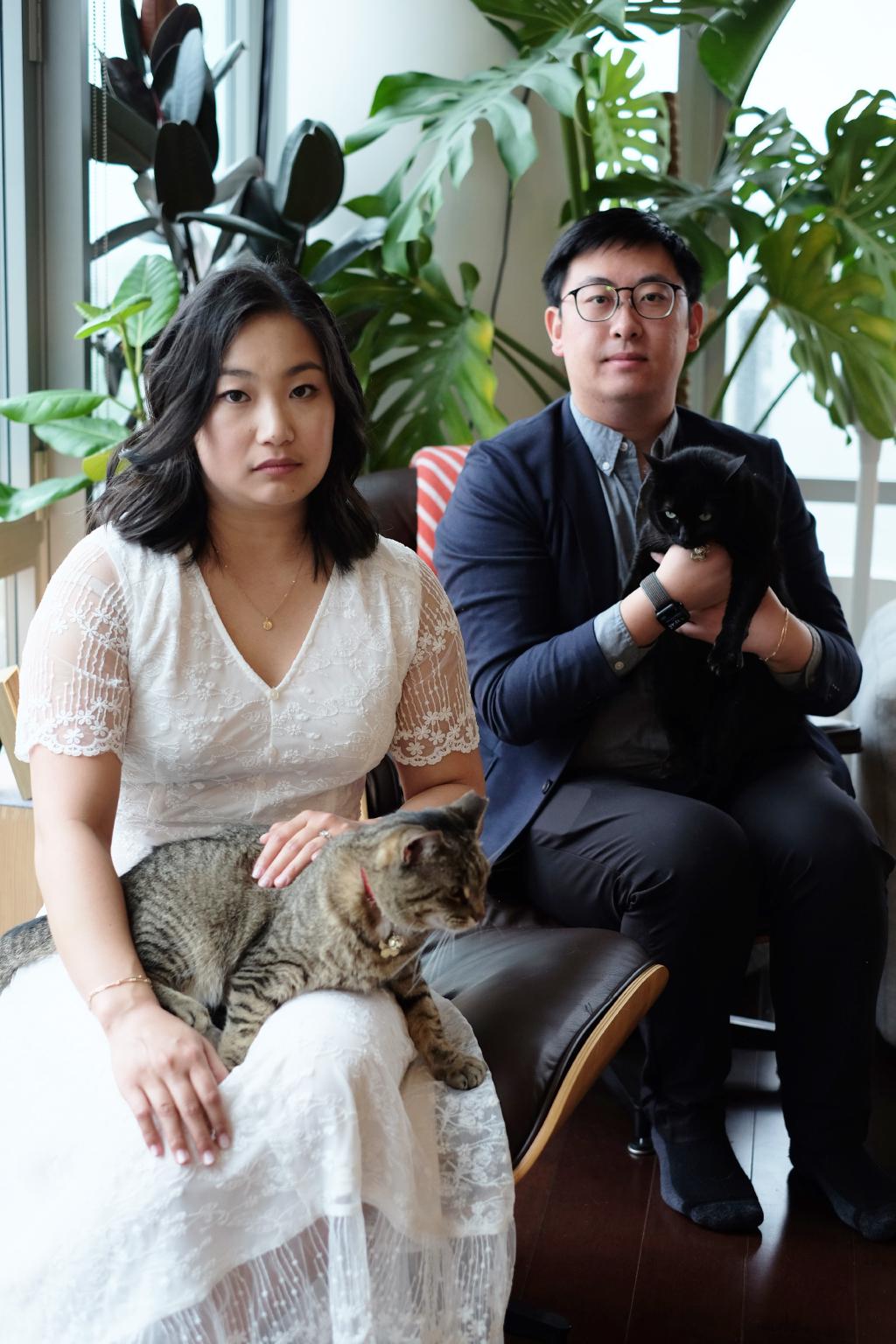 Kelly and Eric sitting with serious expressions, holding their two cats Peaches and Moon Moon